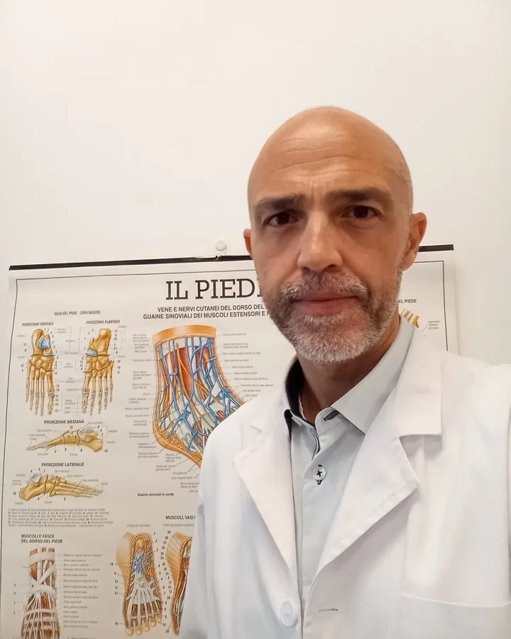 Daniel Michieletto in camice bianco davanti a una tavola anatomica del piede
